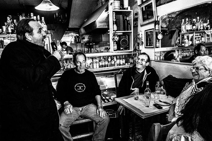 Black and white photograph of a man singing to the seated patrons of Theoklitos Café.