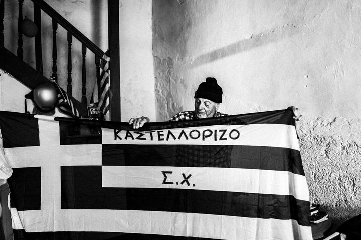 Black and white photograph of Stavros Choulis holding a Greek flag in Kastellorizo.