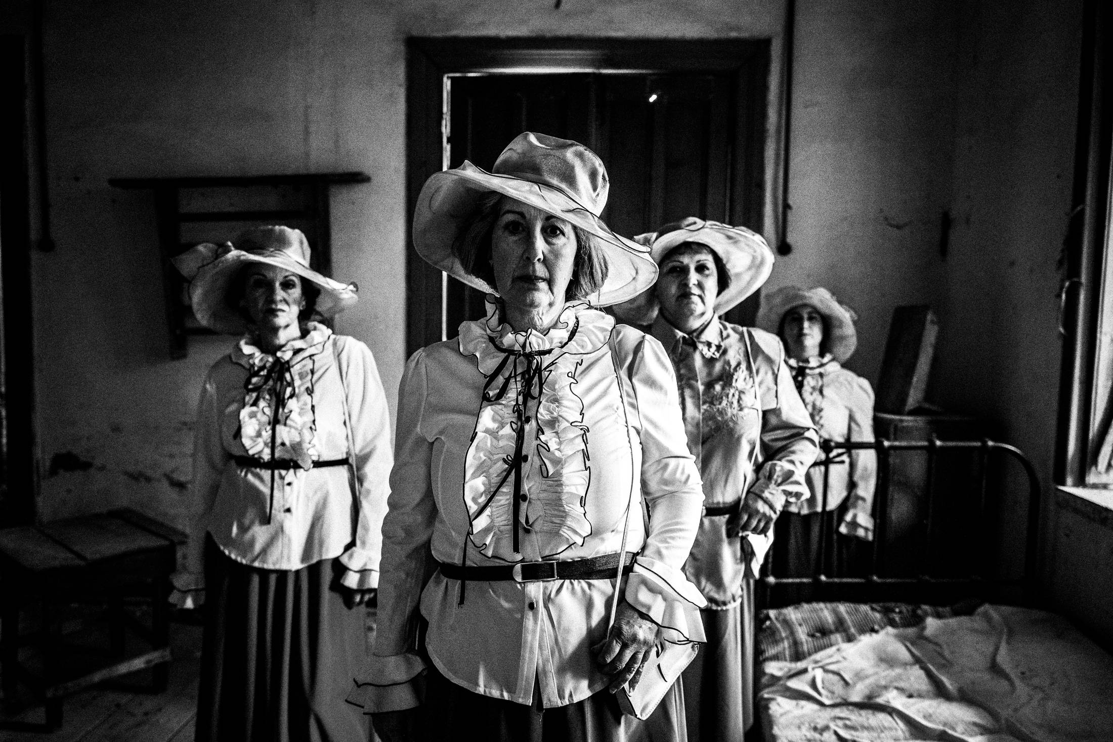 Four women standing amongst the ruins of a local leprosarium, wearing the urban dresses of Kofinas, Chios.