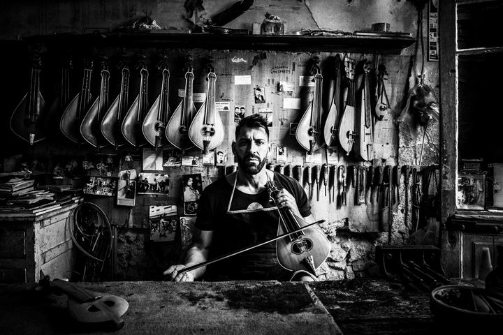 Black and white photograph of Nikos Papalexakis playing the Cretan lyre inside his workshop in Rethymnon, Crete.