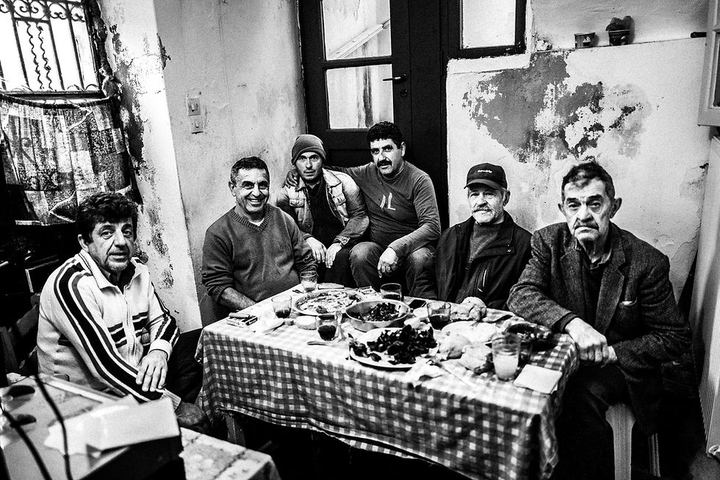 Black and white photograph of men gathered around a table inside the house of the Verikokos family in Naxos.