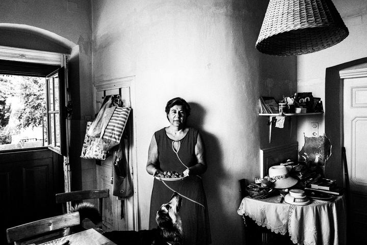 Black-and-white photograph of Xanthippi holding a plate of Fylla inside a house on Kalymnos.