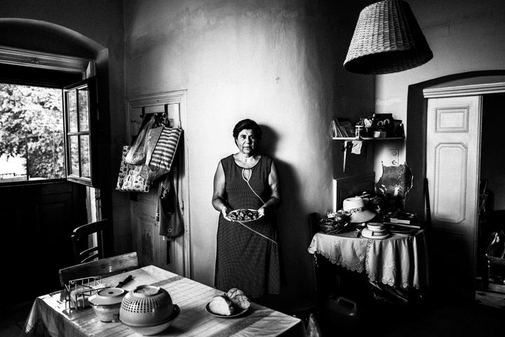 Black-and-white photograph of Xanthippi holding a plate of Fylla inside a house on Kalymnos.