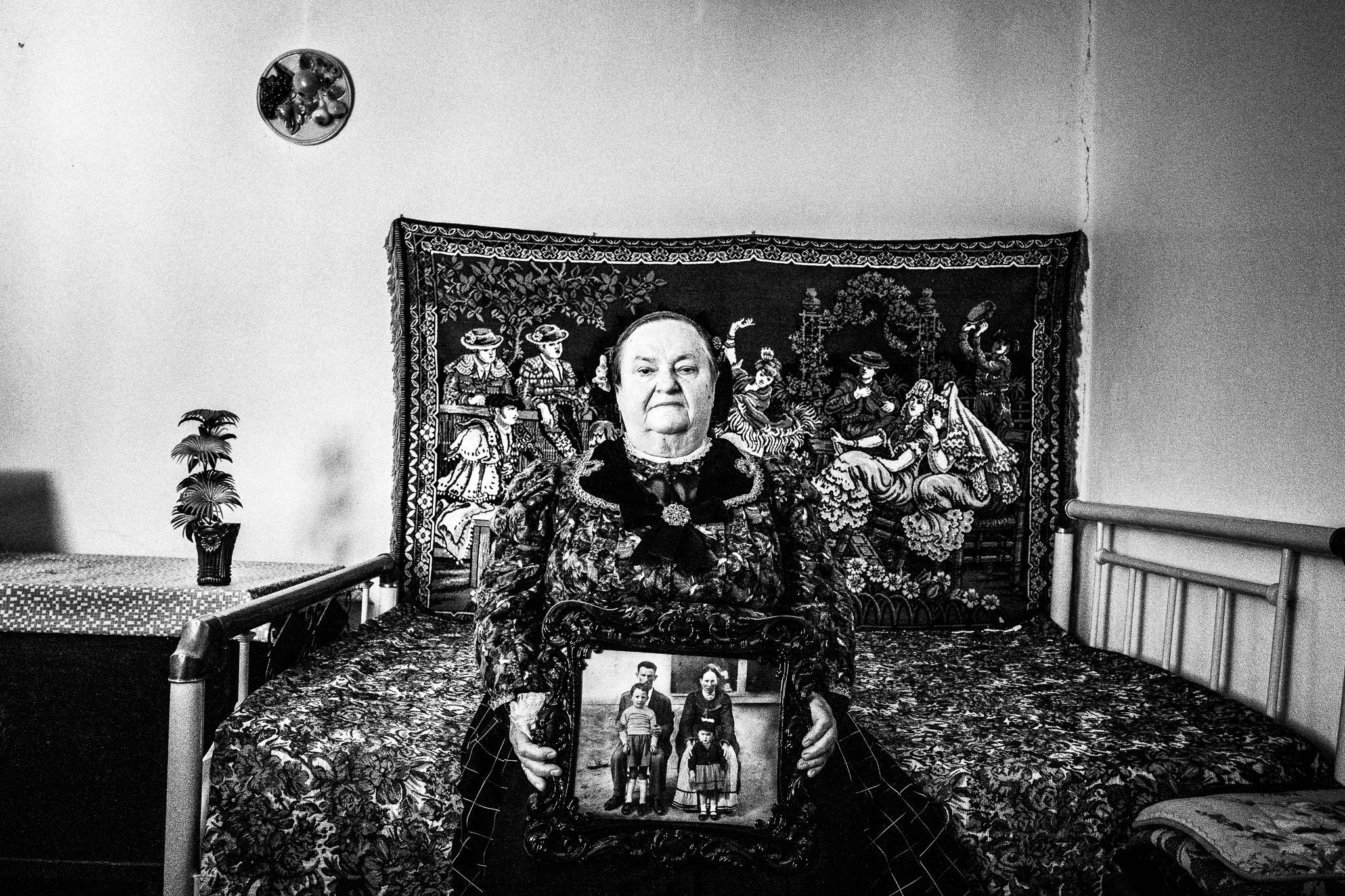 Woman wearing the local costume of Nea Vyssa in Evros, sitting on a bed, holding an old family photo.