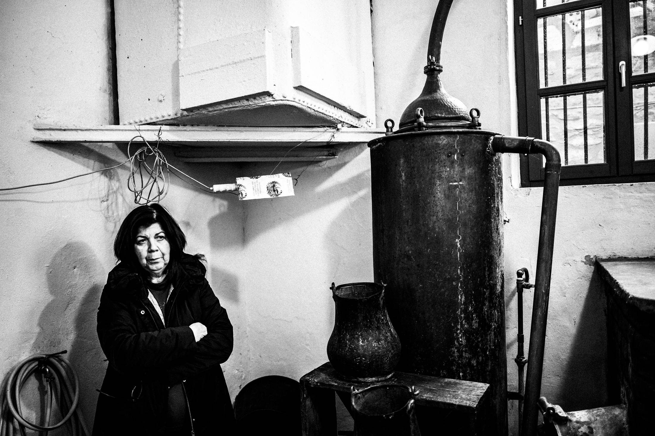 Black and white photograph of the distillery owner standing beside a traditional copper still in Naxos.