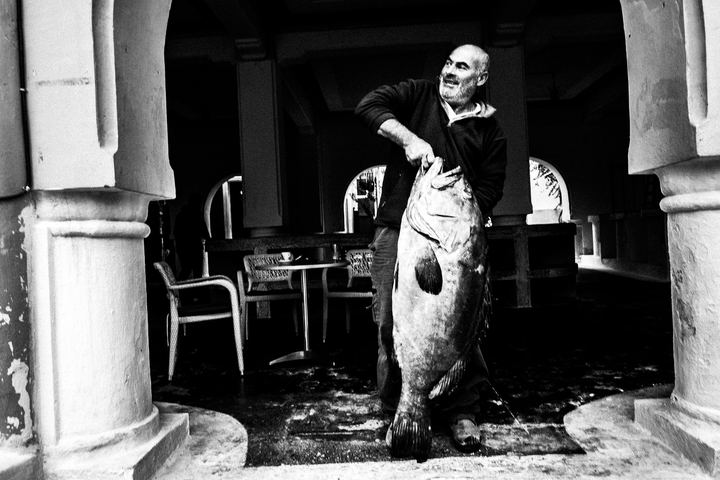Black and white photograph of a local fisherman holding his catch in Kastellorizo.