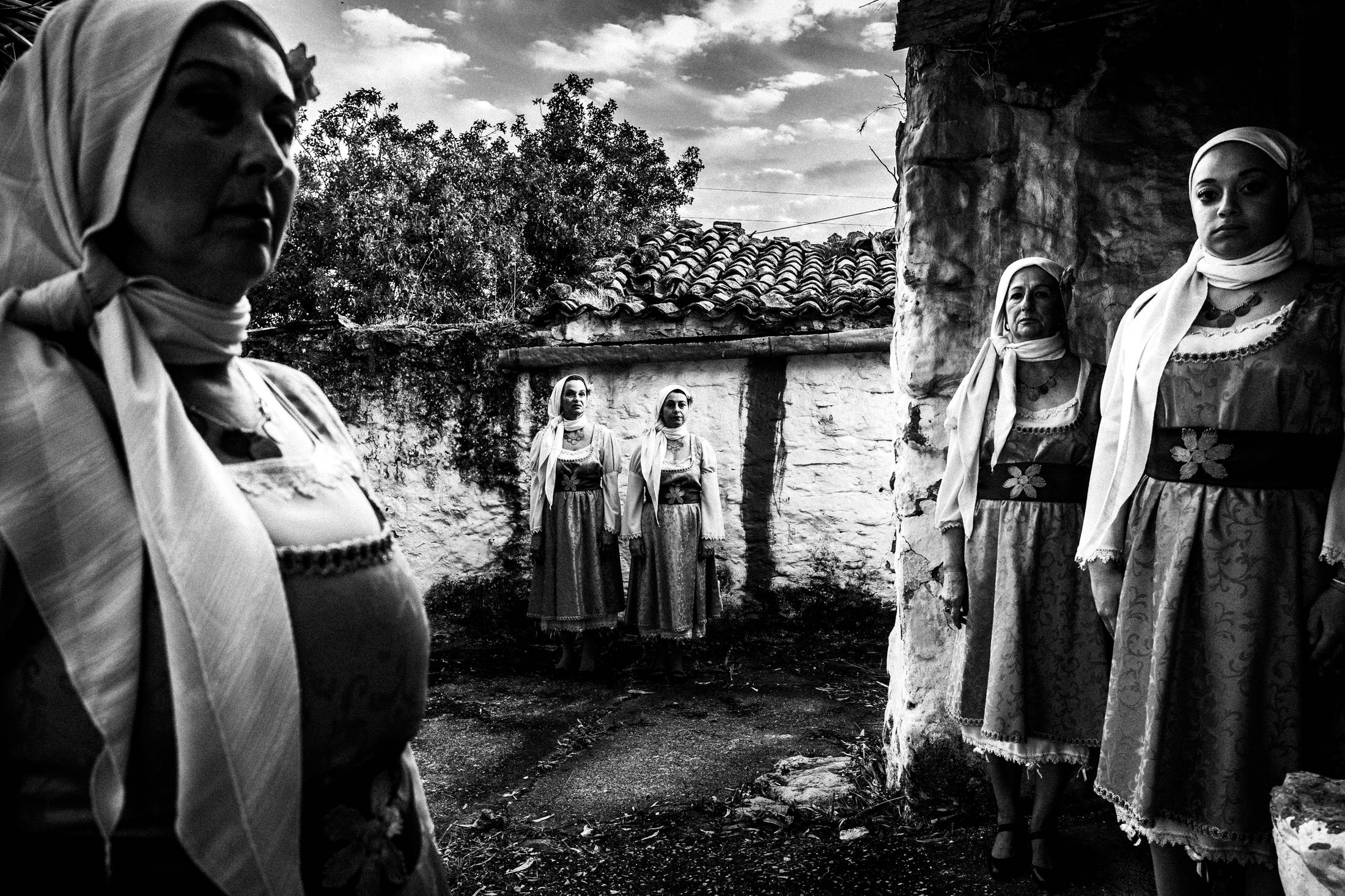 Five women standing in a backyard, wearing the local urban dresses of Vassileoniko in Chios