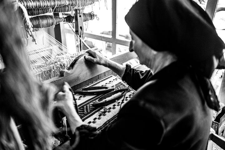 Black and white photograph from behind Hermione as she works carefully at the loom.