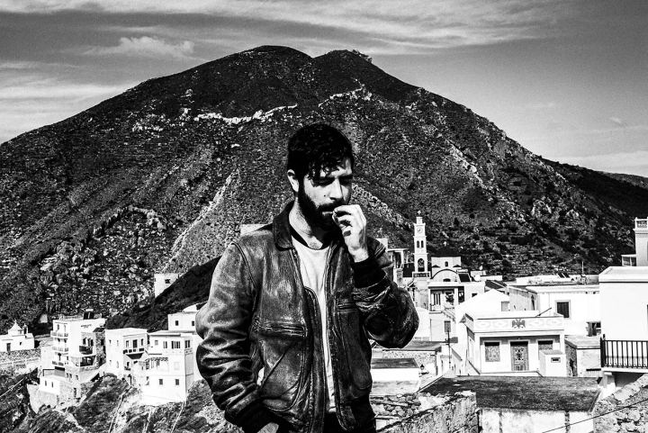 Black and white photograph of Yannis Philippakis in Olympos with the church tower and mountains in the background.
