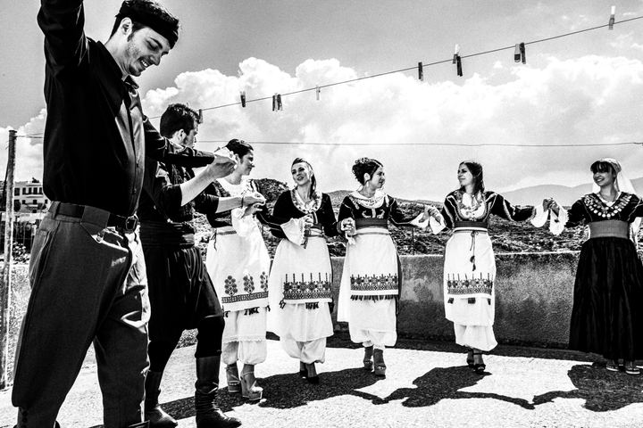 Black and white photograph of people dancing on a rooftop before a wedding in Anogia, Crete.
