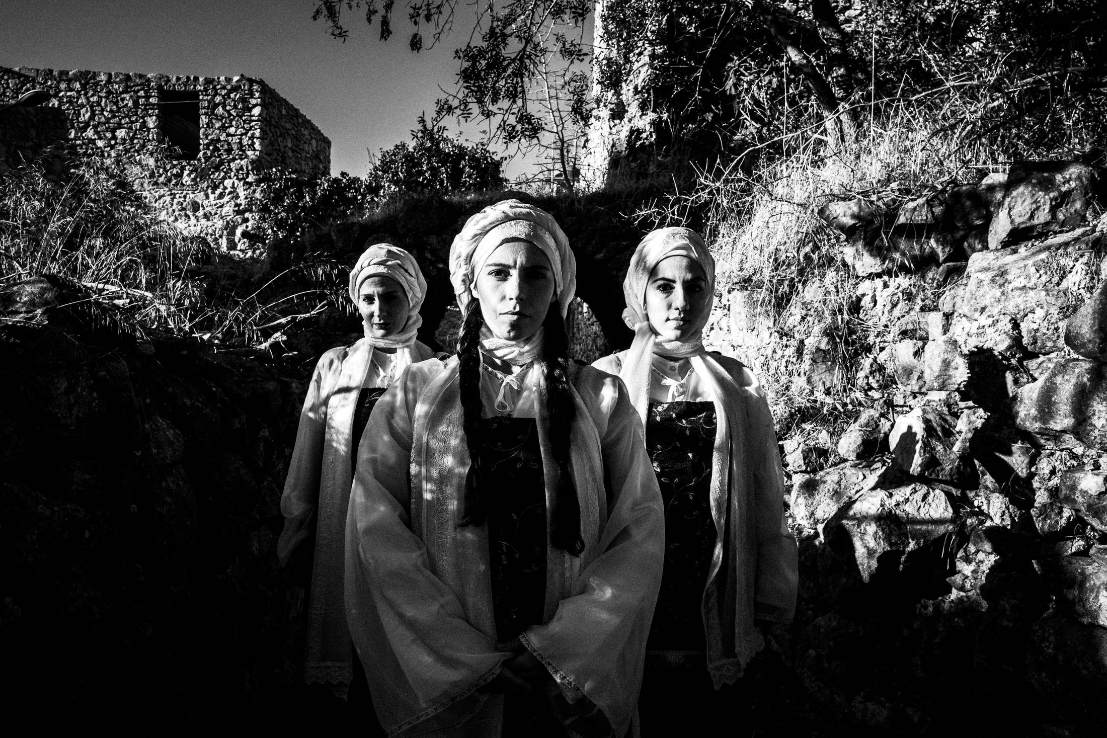 Three women in formation, wearing the local dresses of Vessa in Chios, standing in the sun