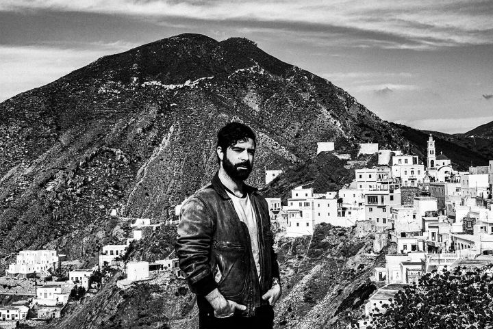 Black and white photograph of Yannis Philippakis standing before Olympos and the surrounding mountains.