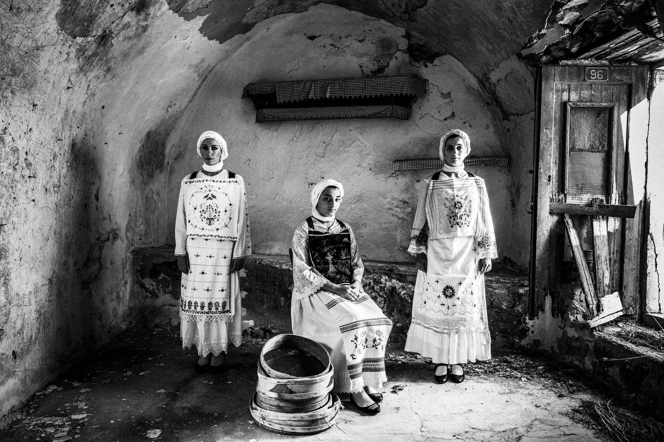 Three women wearing the local costumes of Lithi on the island of Chios, standing inside an old local house.