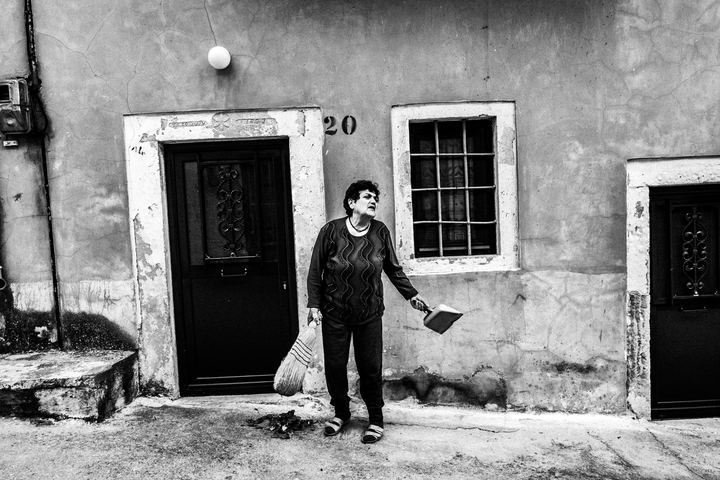 Black and white photograph of a woman sweeping a courtyard in Patrika, Chios.