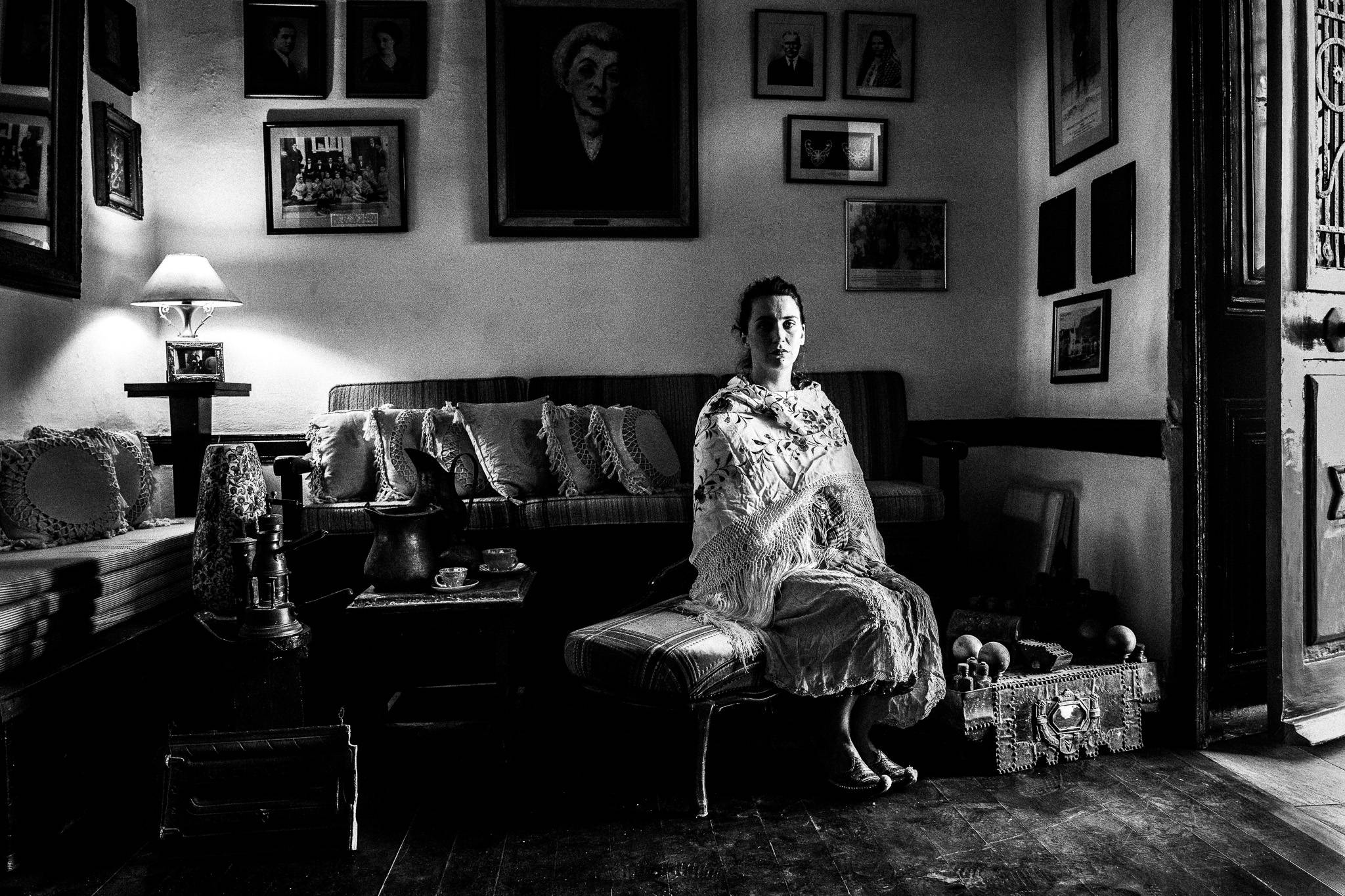 A woman wearing the local costume of Kastellorizo, sitting in a sofa, inside a local house by the window