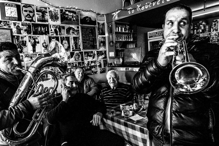 Black and white photograph of brass musicians playing among café tables in Florina.