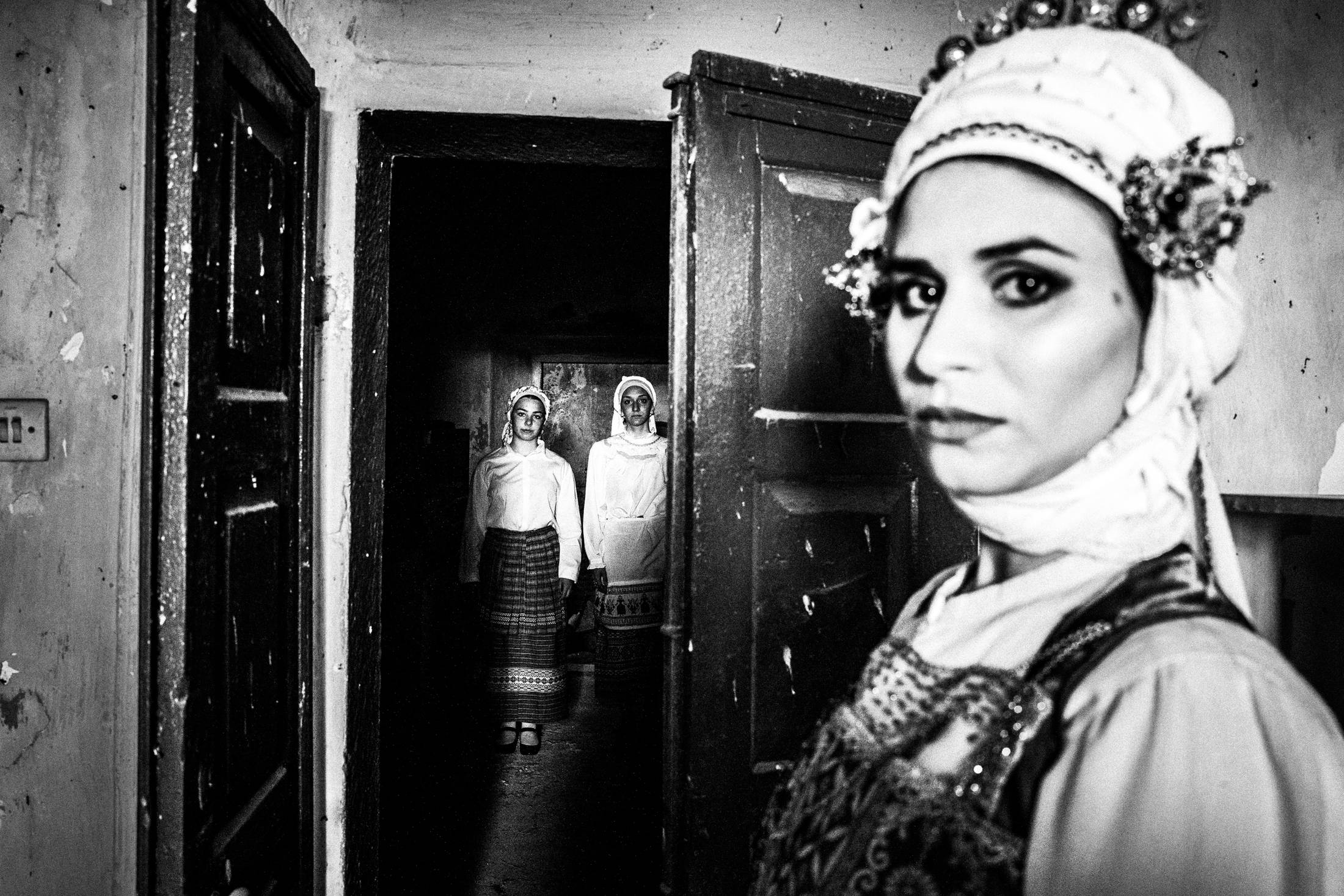 Three women inside an old house, wearing the local dresses of Olympoi, Chios