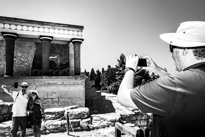 Black and white photograph of visitors at Knossos, Crete, observing the ancient site.