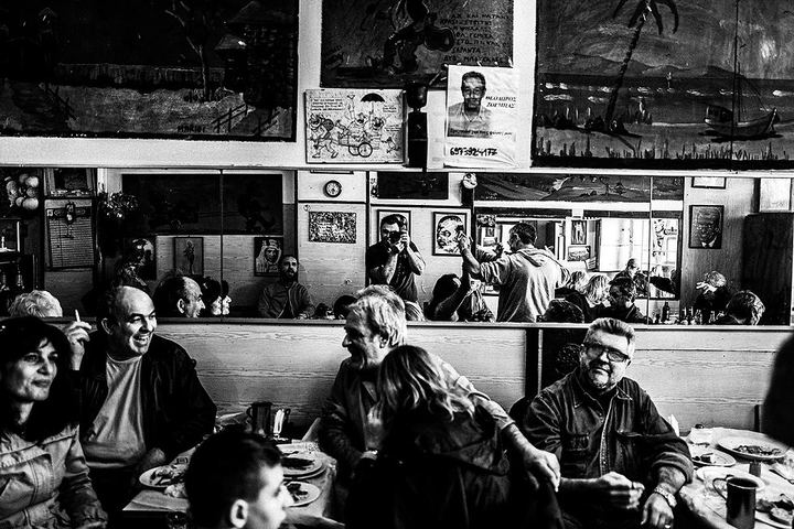 Black and white photograph of people sitting inside Theoklitos Café in Piraeus.