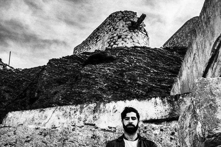 Black and white portrait of Yannis Philippakis below old stone architecture in Olympos.