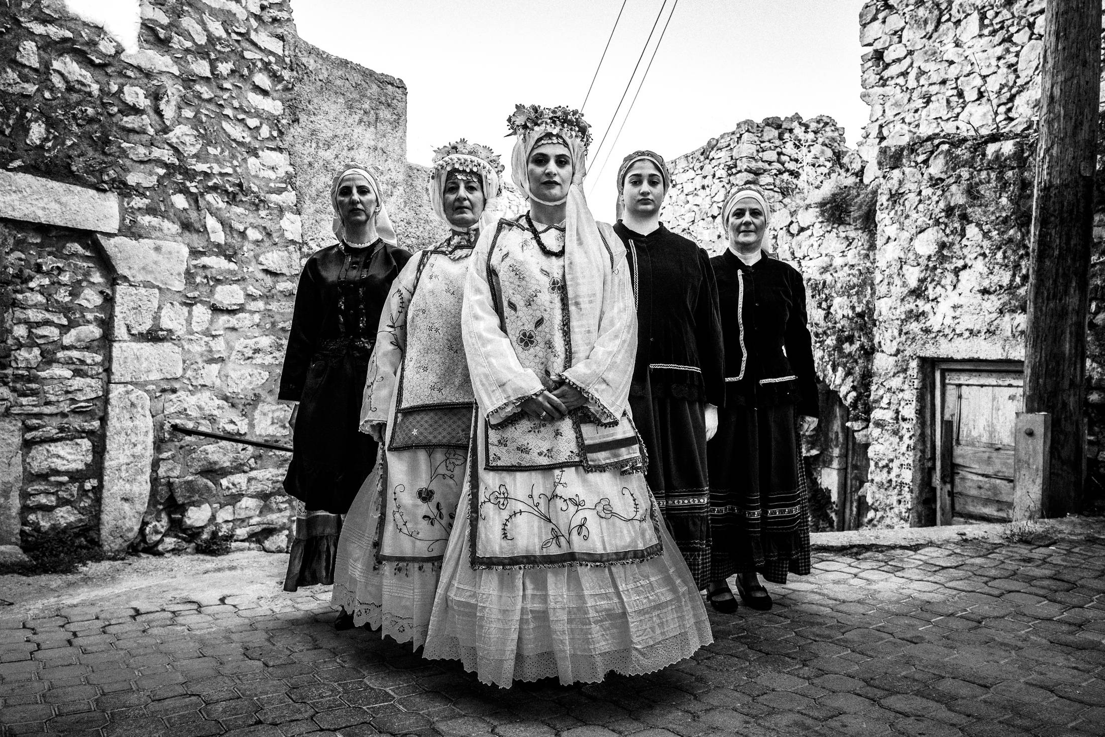 Five women wearing the local costumes of Agios Georgios Sykoussis, standing in formation inside the village