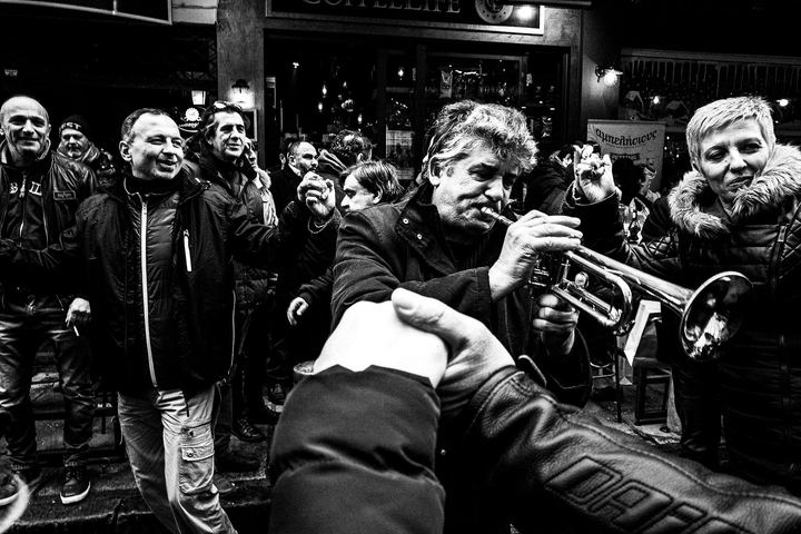 Black and white photograph of brass musicians playing among people at Kapani Market in Thessaloniki.