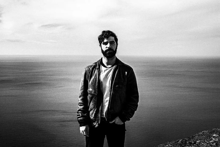 Black and white portrait of Yannis Philippakis standing above the sea near Olympos.