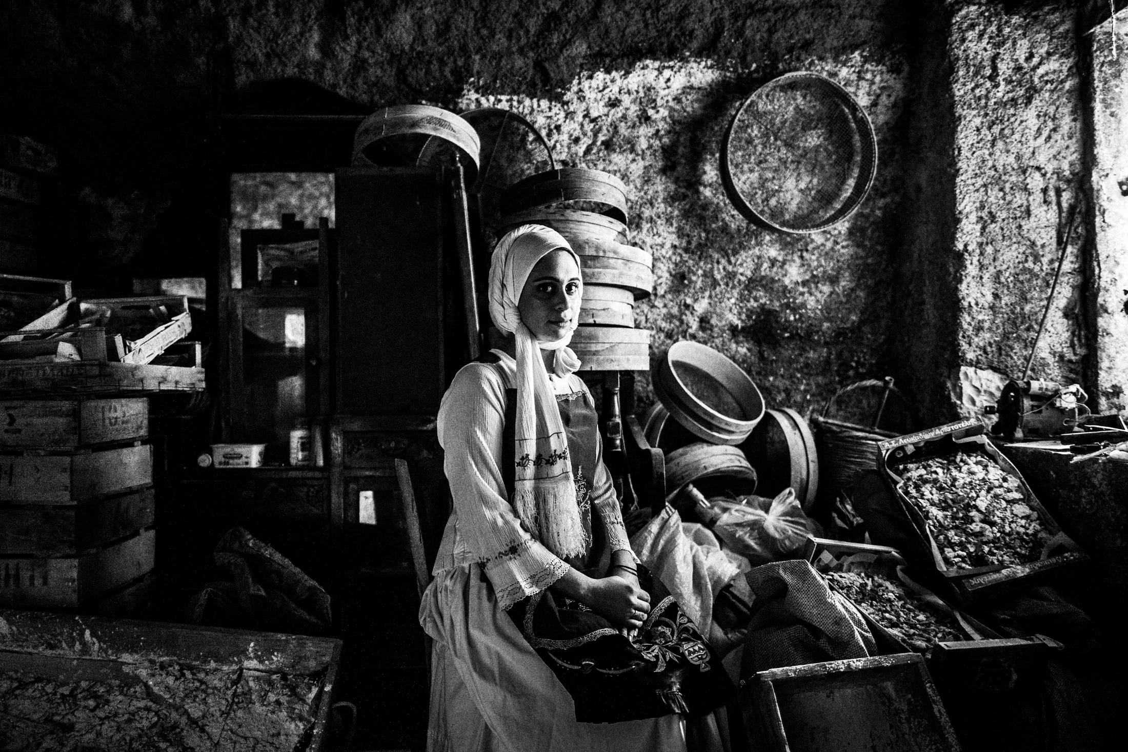 A woman wearing the local dress of Nenita, Chios, sitting inside a warehouse that stores mastic and related tools.