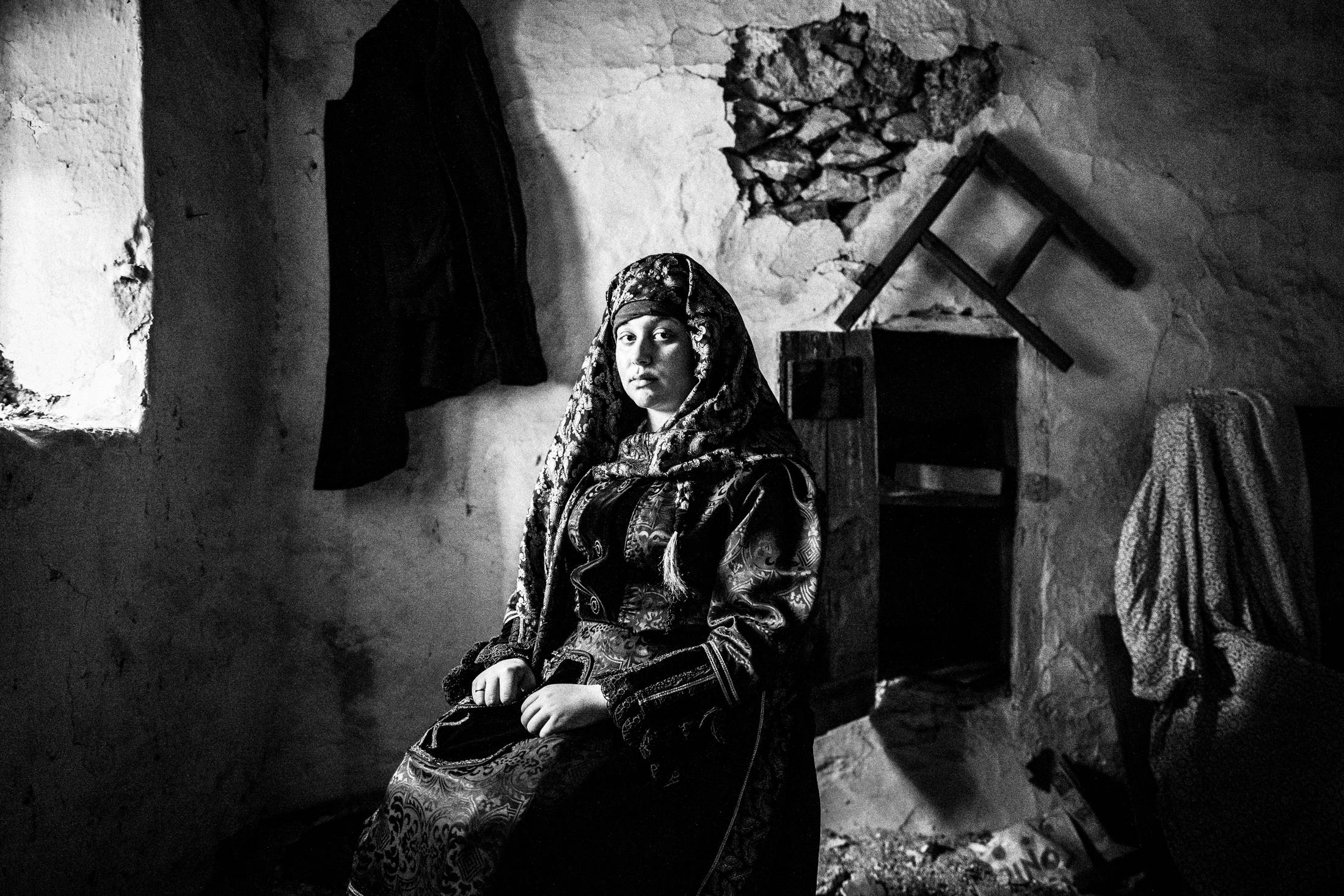 A woman, sitting by a window, in an old abandoned local house, wearing the traditional costume of Kardamyla