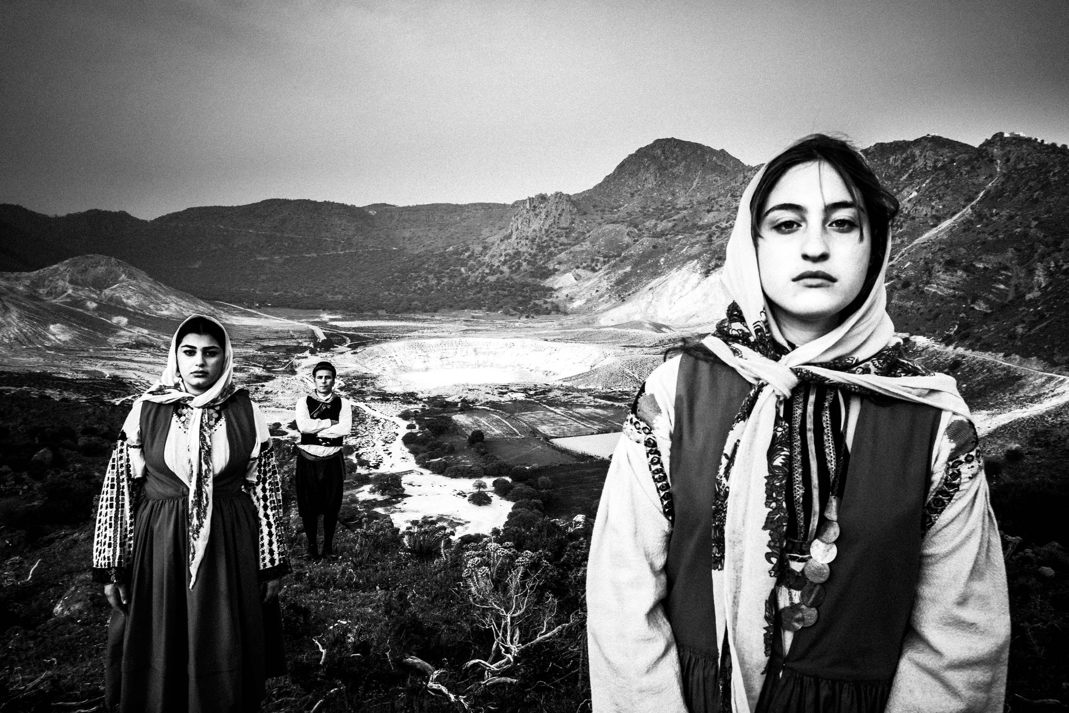 A man and two women wearing the costumes of Nisyros, stand by the volcano