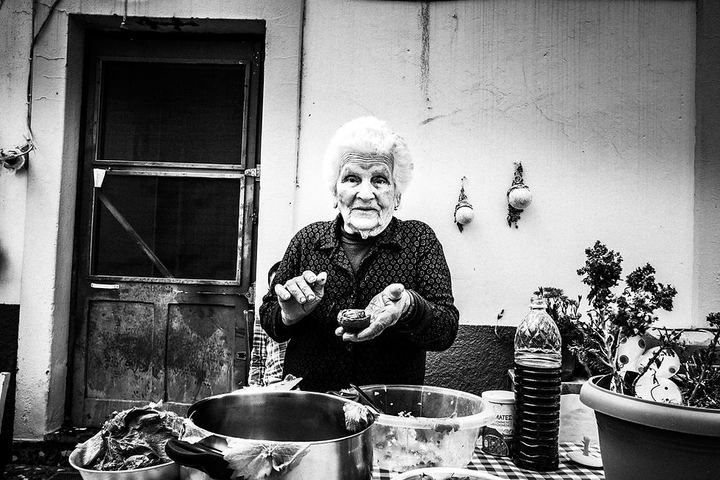 Black and white photograph of Chryssi preparing giaprakia outside her home in Patmos.