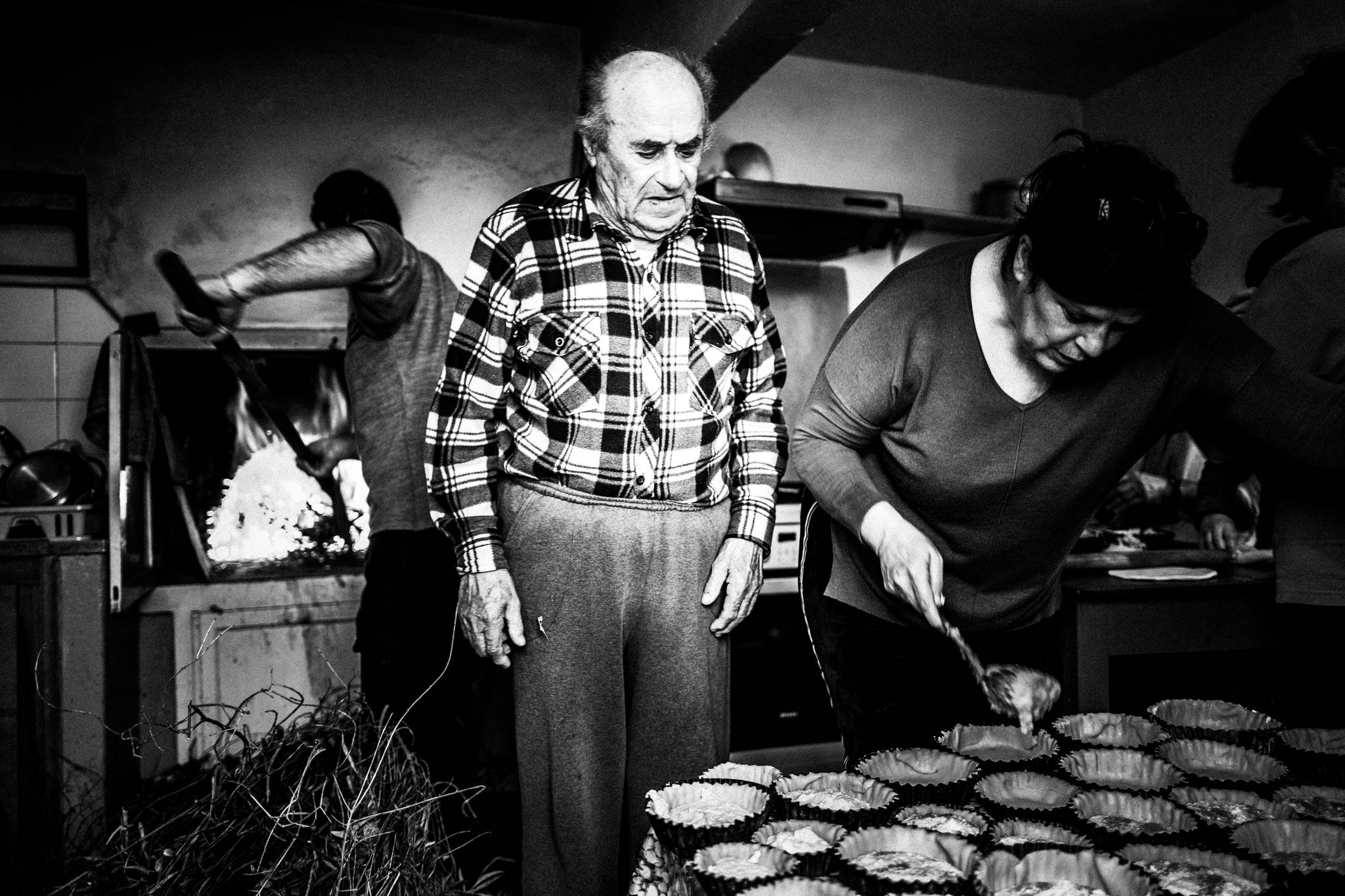 Black and white photograph of the Gryllis family preparing Patiniotikes pies around a traditional oven.