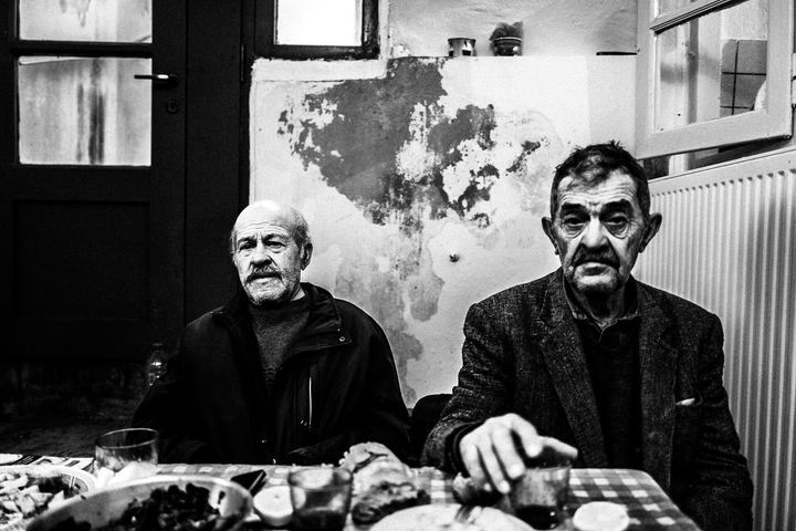 Black and white photograph of men talking during lunch inside the Verikokos family house in Naxos.