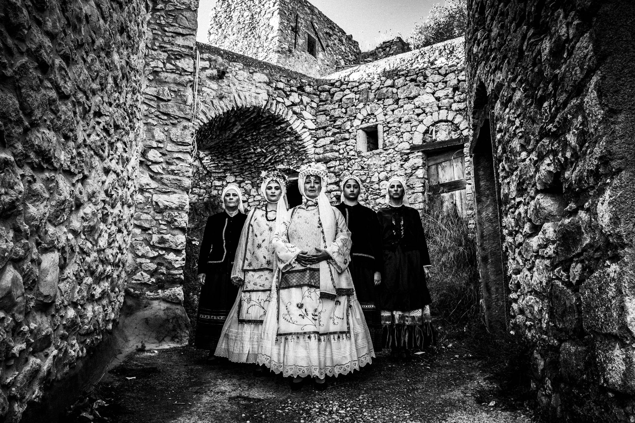 Five women standing in formation around the village of Agios Georgios Sykoussis, wearing the local costumes
