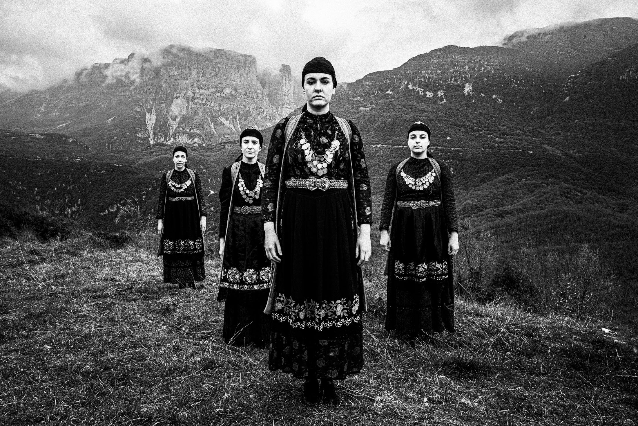 Four women wearing the traditional costumes of Zagori, standing on a hill at Agios minas, overlooking the mountains of Papiggo