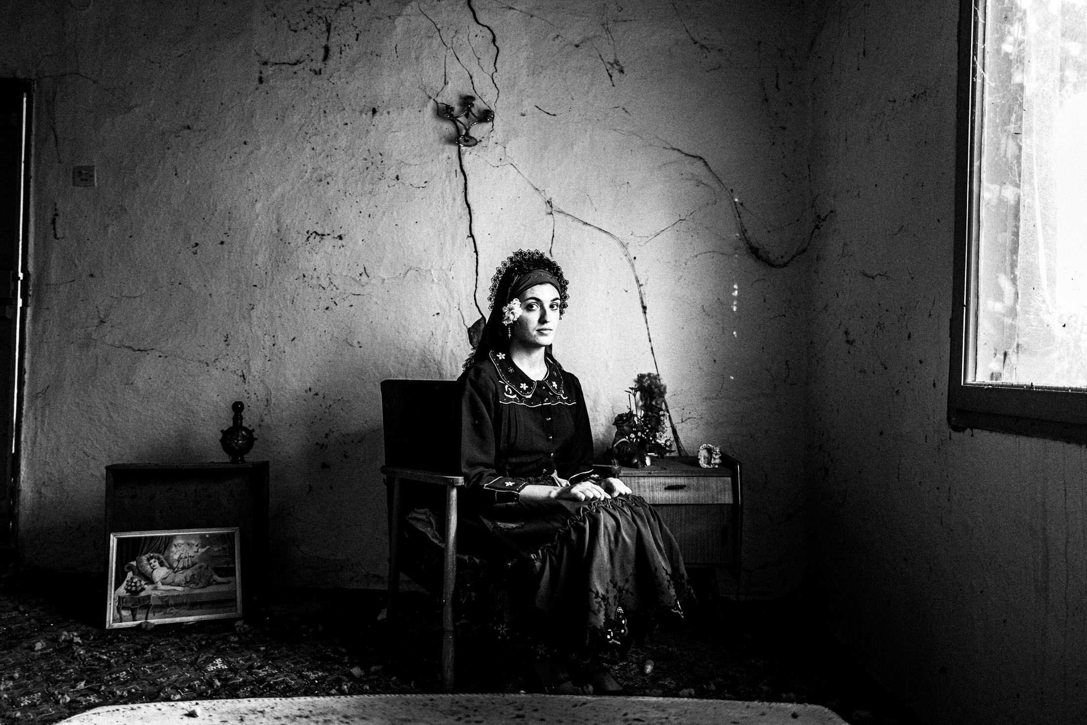 A woman wearing the local dress of Enoe in Orestiada, sitting inside an old local house by the window