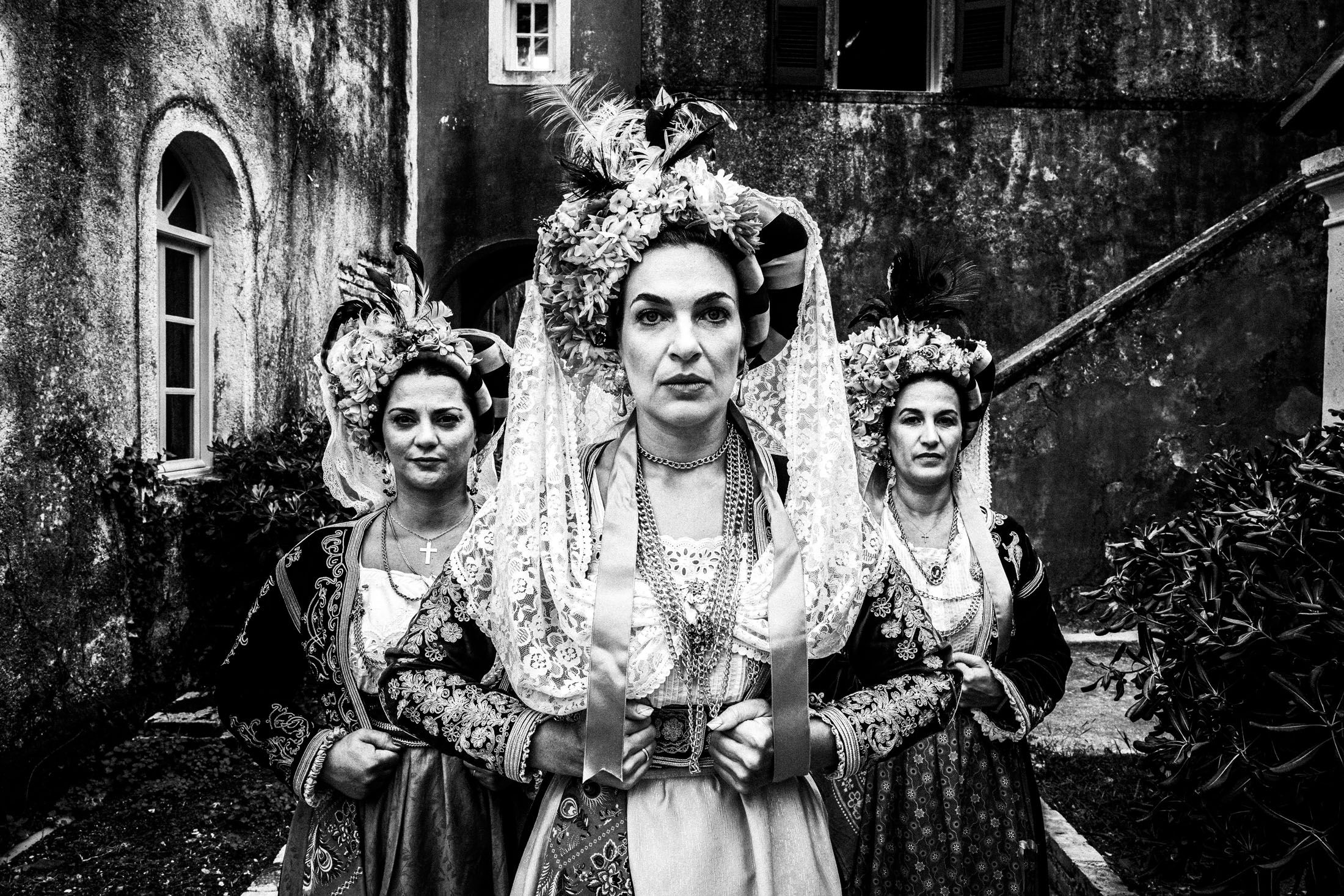 Three women in the costumes of Central Corfu posing in formation in a traditional local settlement