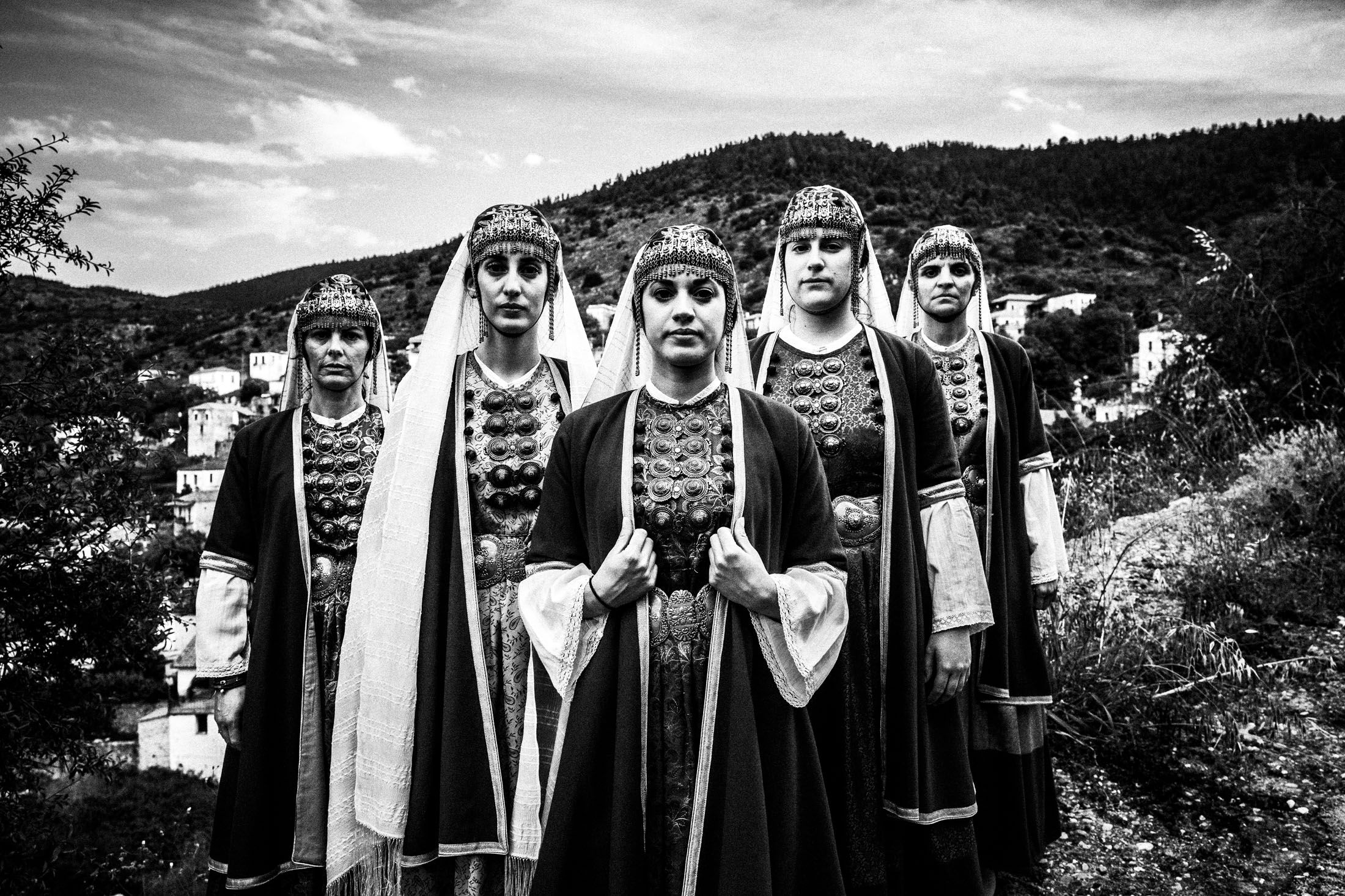 Five women wearing the local costumes of Prastos, Arcadia, standing in formation overlooking the village.