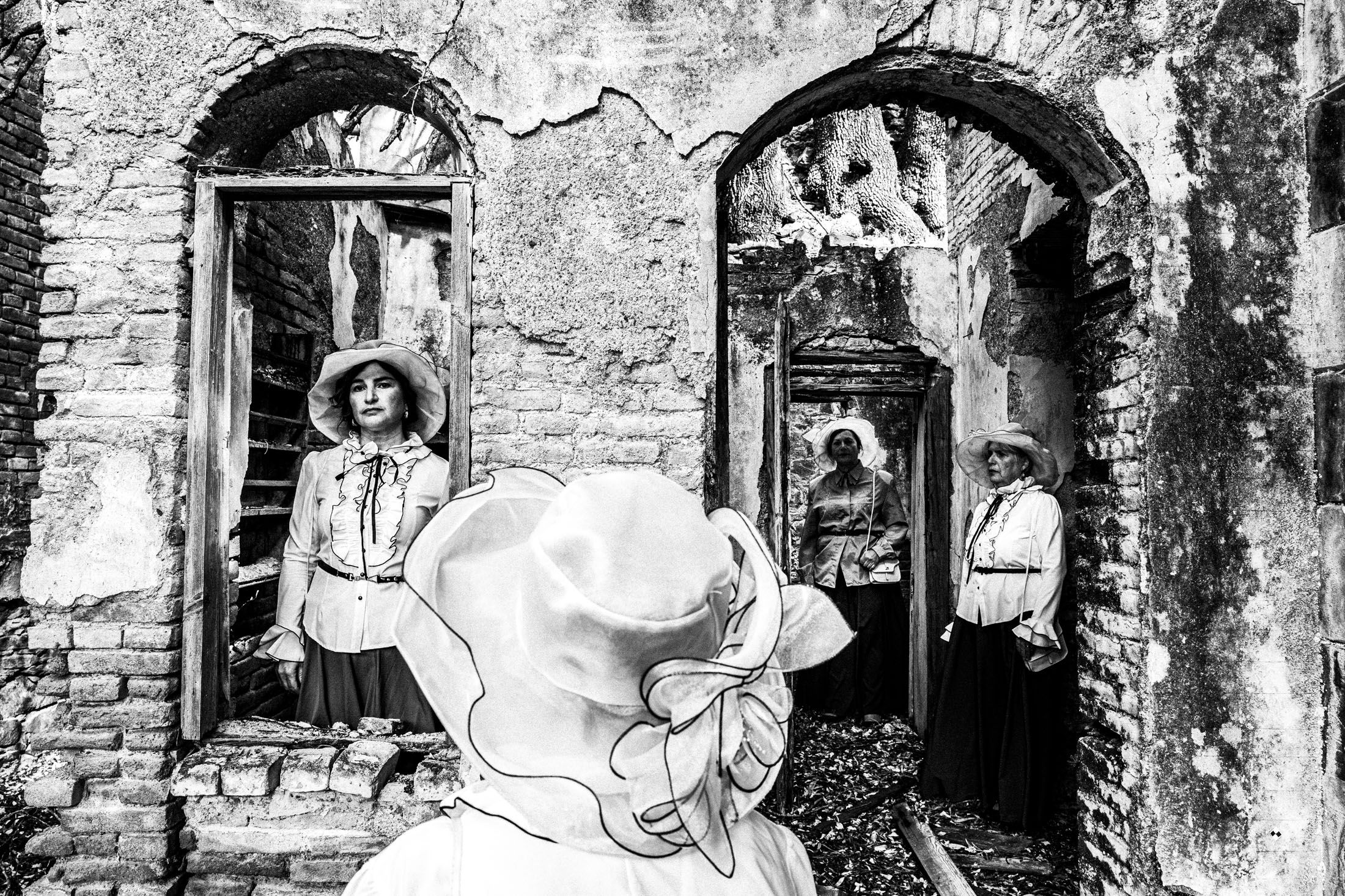Four women standing amongst the ruins of a local leprosarium, wearing the urban dresses of Kofinas, Chios.