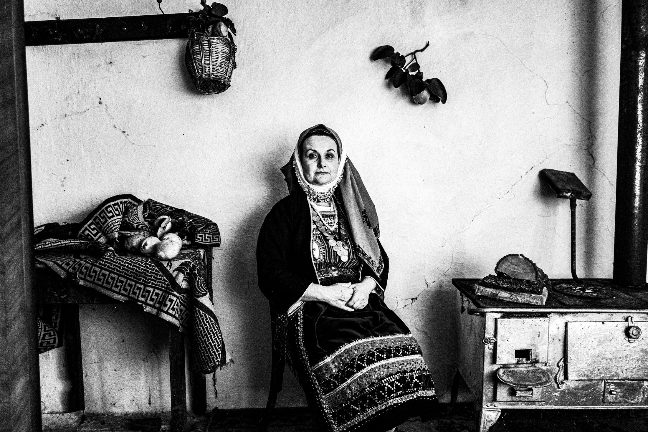 A woman wearing the local costume of Vryssi in Evros, sitting inside a local traditional kitchen.