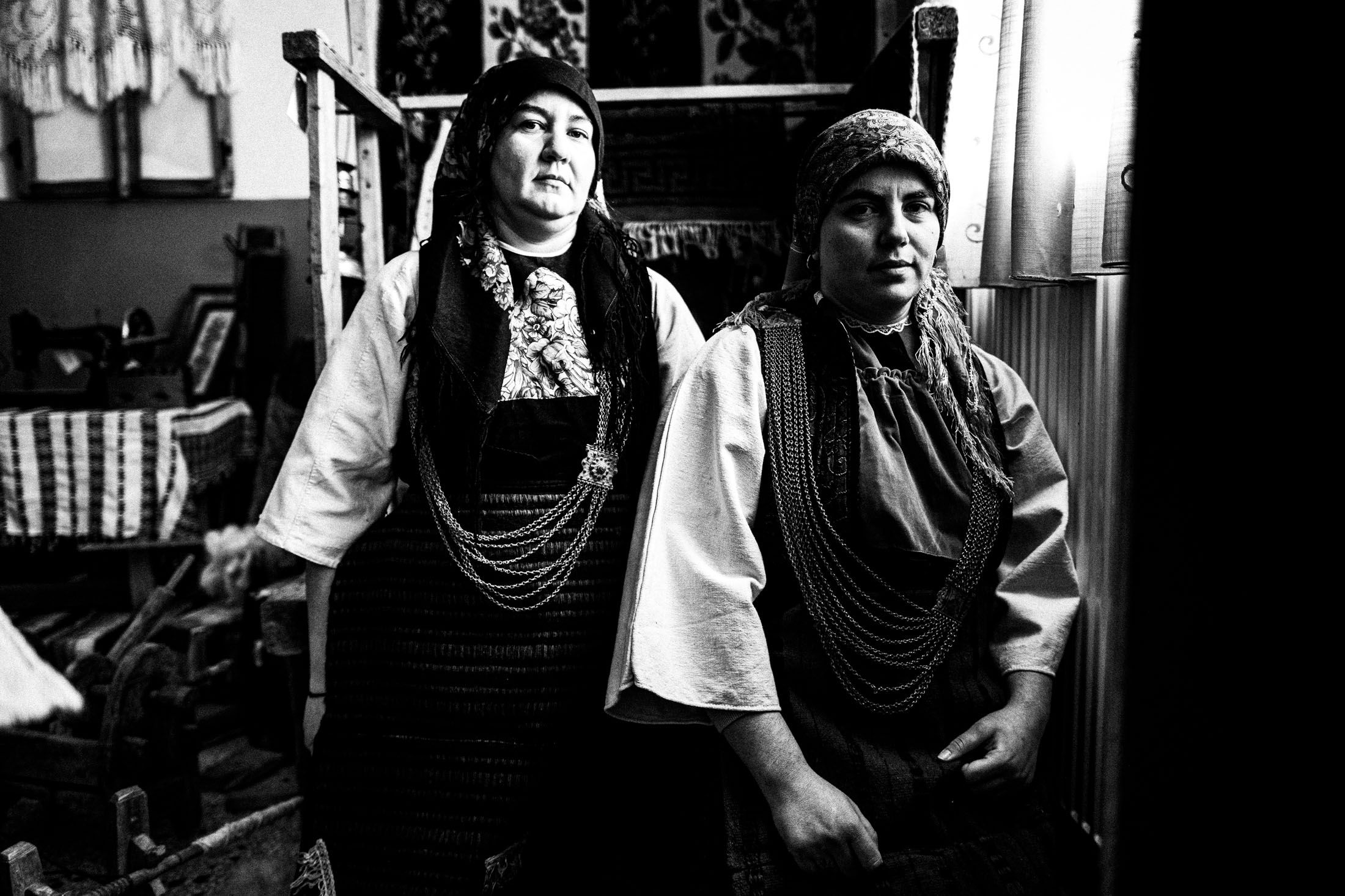Two women in the local dresses of Skopos, Florina are sitting on the ground by a window at the local folklore museum